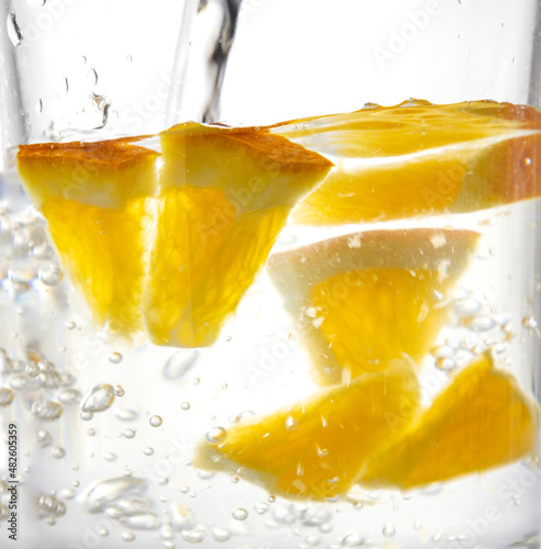 Fresh tatsy pieces of oranges and pouring water.Fresh summer drink photo