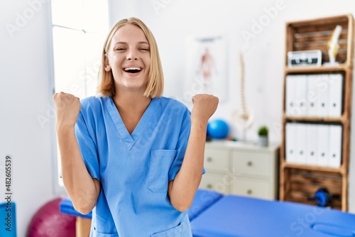 Young caucasian physiotherapist woman working at pain recovery clinic screaming proud, celebrating victory and success very excited with raised arms