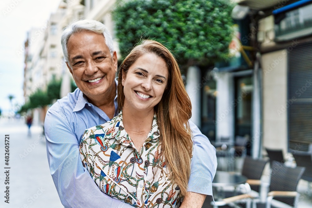 Middle age hispanic couple of husband and wife together on a sunny day outdoors. Smiling happy in love hugging at the city