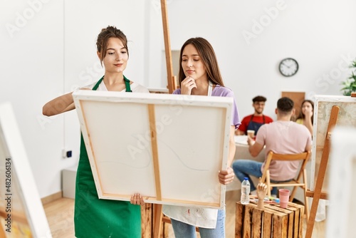 Group of people drawing sitting on the table. Two women smiling happy holding canvas at art studio.
