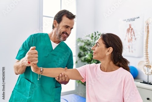 Middle age man and woman smiling confident stretching arm having rehab session at physiotherapy clinic