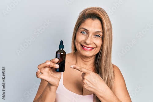 Middle age hispanic woman using night serum smiling happy pointing with hand and finger