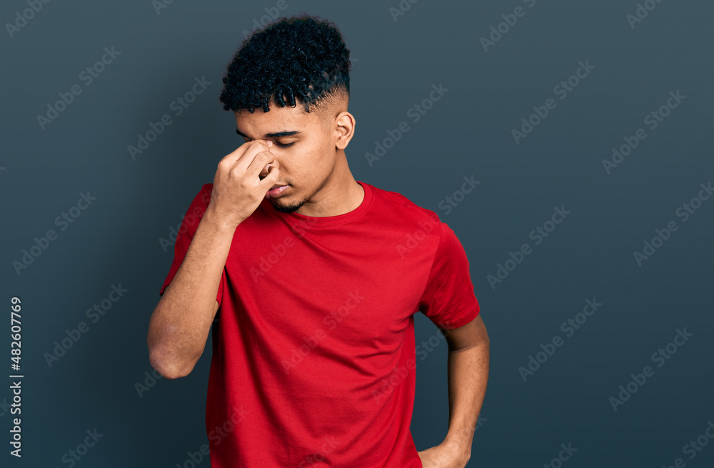 Young african american man wearing casual red t shirt tired rubbing nose and eyes feeling fatigue and headache. stress and frustration concept. Young african american man wearing casual red t shirt tired rubbing nose and eyes feeling fatigue and headache. stress and frustration concept.