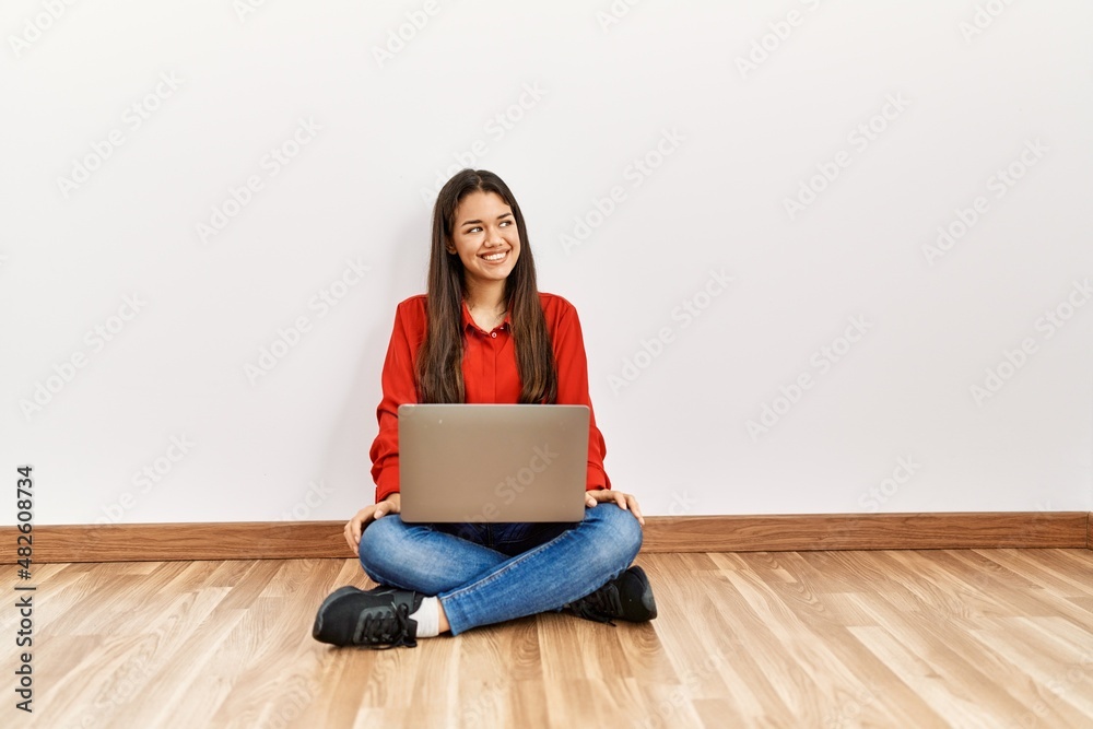Young brunette woman sitting on the floor at empty room with laptop looking away to side with smile on face, natural expression. laughing confident. Young brunette woman sitting on the floor at empty room with laptop looking away to side with smile on face, natural expression. laughing confident.