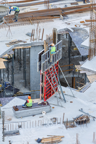 Building construction site work against blue sky.Hydraulic luffing jib tower cranes and workers being poured concrete into foundation. Cement pouring into formwork of building at construction site.