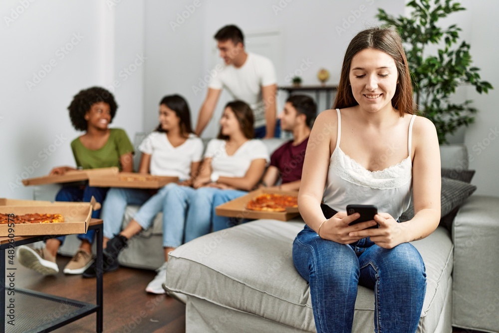 Group of young friends eating italian sitting on the sofa. Woman smiling and using smartphone at home. Group of young friends eating italian sitting on the sofa. Woman smiling and using smartphone at home.