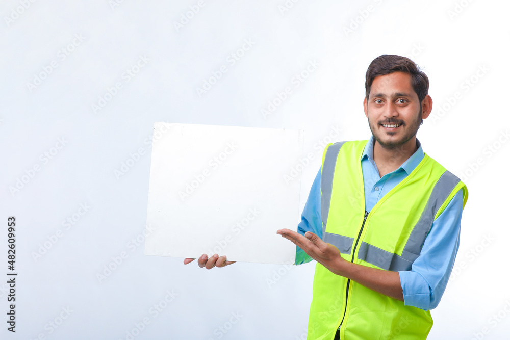 Young indian Construction Worker Showing Empty Poster Board on White Background.