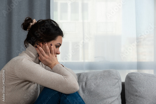 Young sad woman with broken heart sitting alone at home suffering from depression anxiety and bad mental condition. Female having hard time and burnout of overthinking and worry  photo