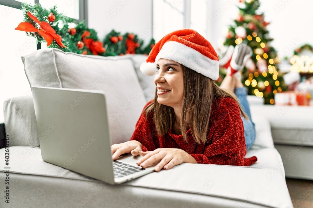 Young hispanic girl using laptop lying on the sofa by christmas tree at home. Young hispanic girl using laptop lying on the sofa by christmas tree at home.