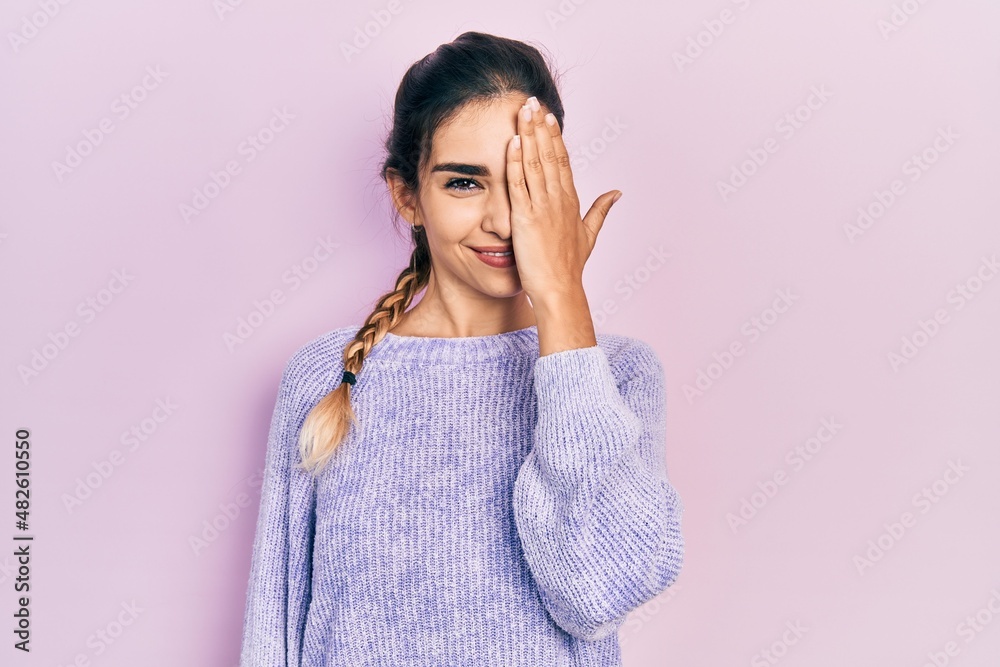 Young hispanic girl wearing casual clothes covering one eye with hand, confident smile on face and surprise emotion. Young hispanic girl wearing casual clothes covering one eye with hand, confident smile on face and surprise emotion.
