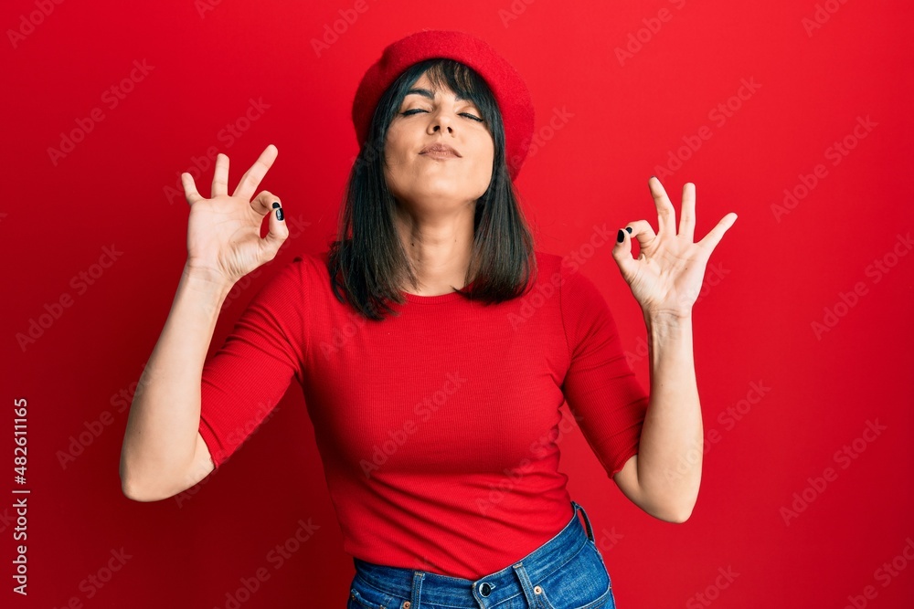 Young hispanic woman wearing french look with beret relax and smiling with eyes closed doing meditation gesture with fingers. yoga concept. Young hispanic woman wearing french look with beret relax and smiling with eyes closed doing meditation gesture with fingers. yoga concept.