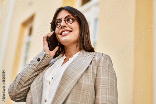 Young hispanic businesswoman smiling happy talking by the smartphone at the city.