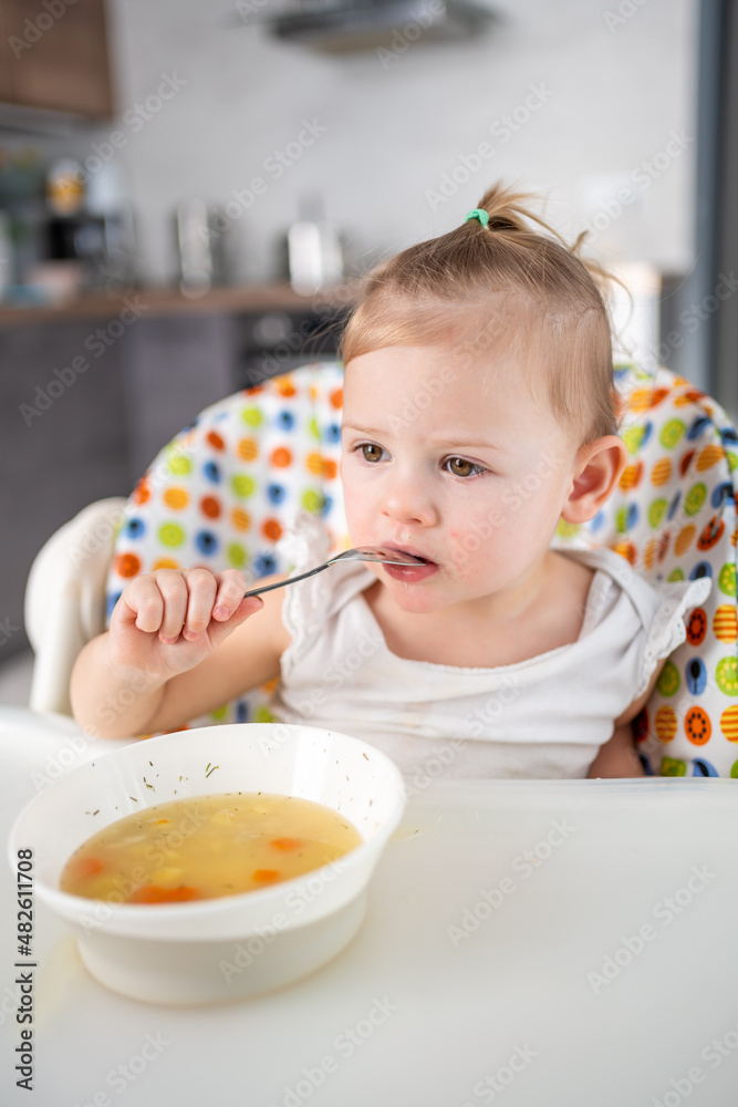 Cute baby girl toddler sitting in the high chair and eating her lunch soup at home kitchen. Cute baby girl toddler sitting in the high chair and eating her lunch soup at home kitchen.