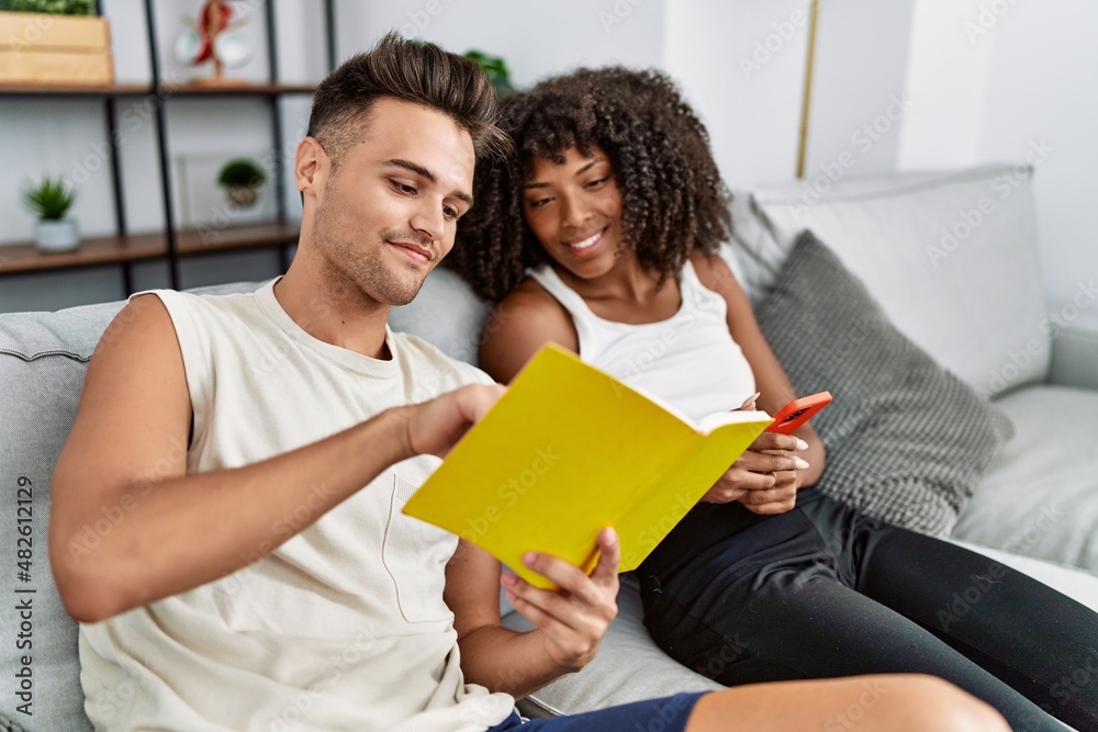 Man and woman couple using smartphone reading book at home