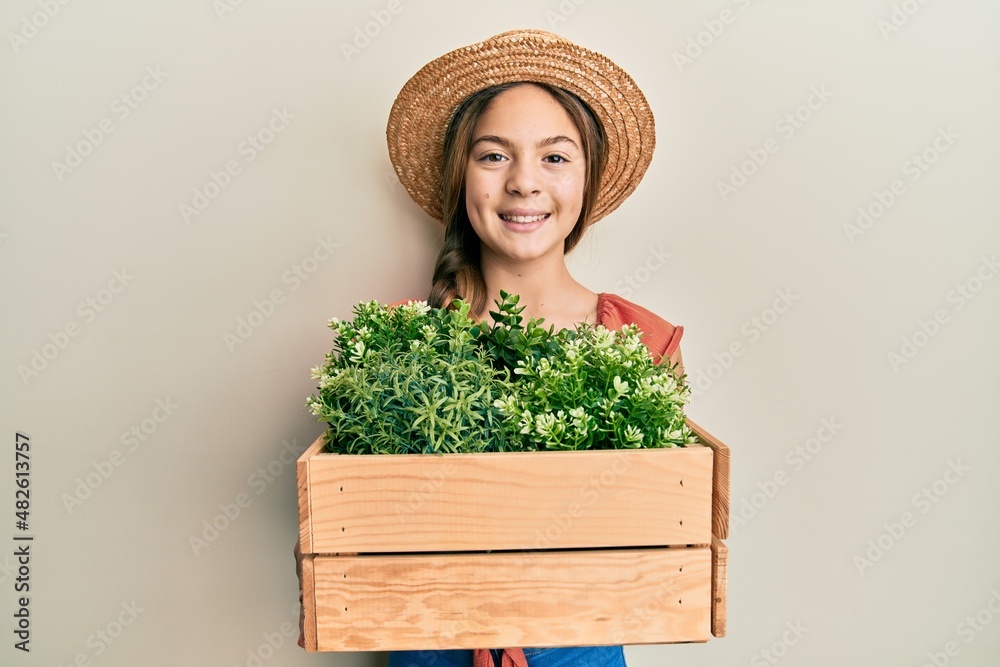 Beautiful brunette little girl wearing gardener hat holding wooden plant pot smiling with a happy and cool smile on face. showing teeth.