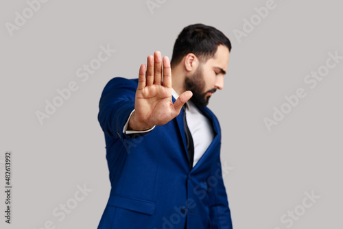 Bearded man making stop gesture showing palm of hand and turning head aside, conflict prohibition warning about danger, stop bullying. Indoor studio shot isolated on gray background. photo