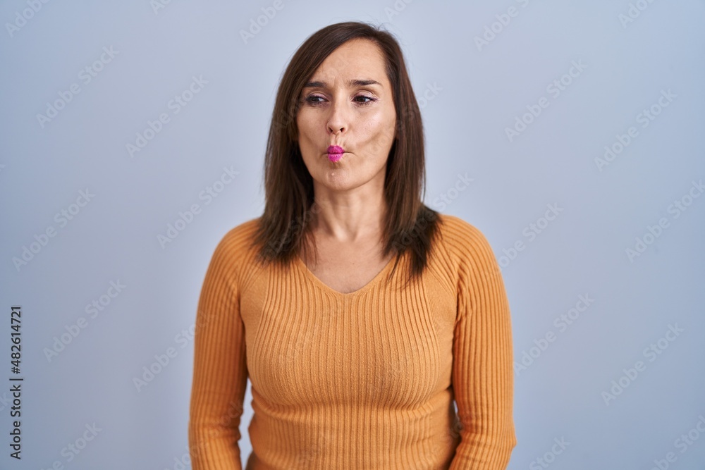 Middle age brunette woman standing wearing orange sweater making fish face with lips, crazy and comical gesture. funny expression. Middle age brunette woman standing wearing orange sweater making fish face with lips, crazy and comical gesture. funny expression.