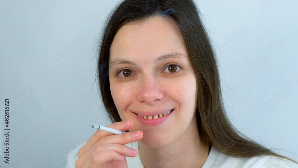 Young woman with yellow bad teeth smoking a cigarrete and smiling looking at camera. Bad habits for dental health, destructive effect of smoking. Ugly smile. Dentistry treatment, prosthetics of teeth. Young woman with yellow bad teeth smoking a cigarrete and smiling looking at camera. Bad habits for dental health, destructive effect of smoking. Ugly smile. Dentistry treatment, prosthetics of teeth.