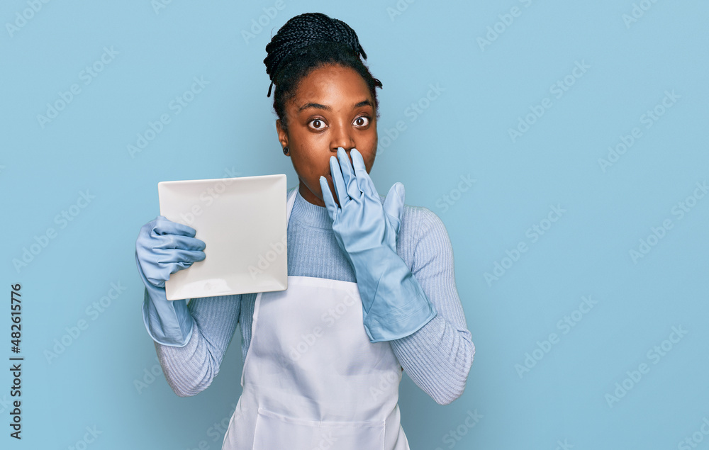 Young african american woman wearing apron washing dishes covering mouth with hand, shocked and afraid for mistake. surprised expression Young african american woman wearing apron washing dishes covering mouth with hand, shocked and afraid for mistake. surprised expression