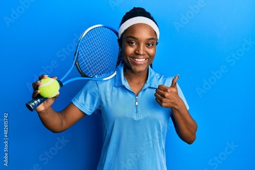 African american woman with braided hair playing tennis holding racket and ball smiling happy and positive, thumb up doing excellent and approval sign © Krakenimages.com