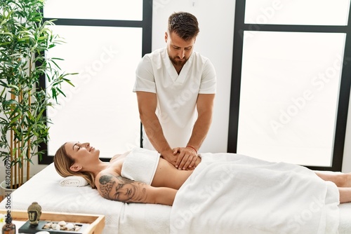 Young caucasian woman at physiotherapy clinic getting muscle massage by professional therapist. Physiotherapist man doing stomach pain treatment to client