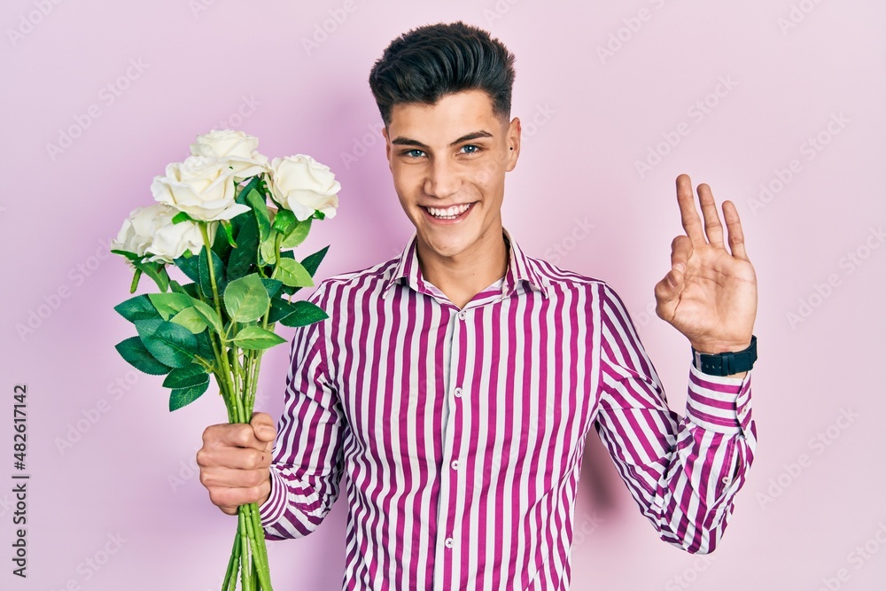Young hispanic man holding flowers doing ok sign with fingers, smiling friendly gesturing excellent symbol Young hispanic man holding flowers doing ok sign with fingers, smiling friendly gesturing excellent symbol