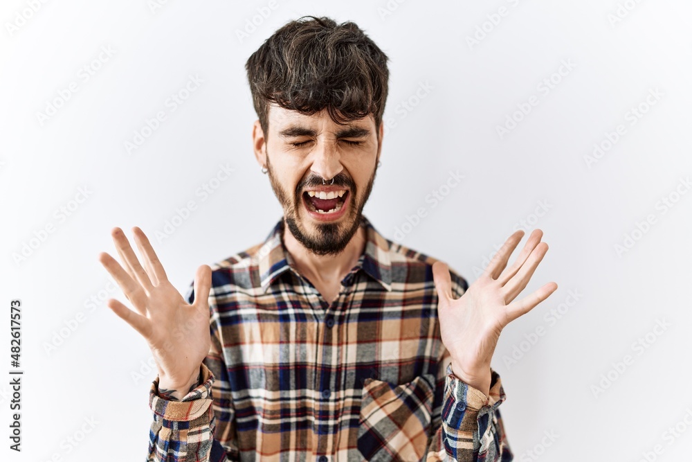 Naklejka premium Hispanic man with beard standing over isolated background celebrating mad and crazy for success with arms raised and closed eyes screaming excited. winner concept