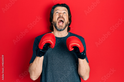 Middle age caucasian man using boxing gloves angry and mad screaming frustrated and furious, shouting with anger looking up.