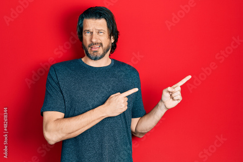 Fotografie Middle age caucasian man pointing with fingers to the side clueless and confused expression