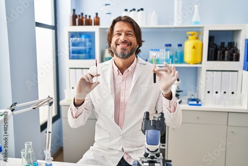 Handsome middle age man holding blood sample at biology laboratory smiling with a happy and cool smile on face. showing teeth.