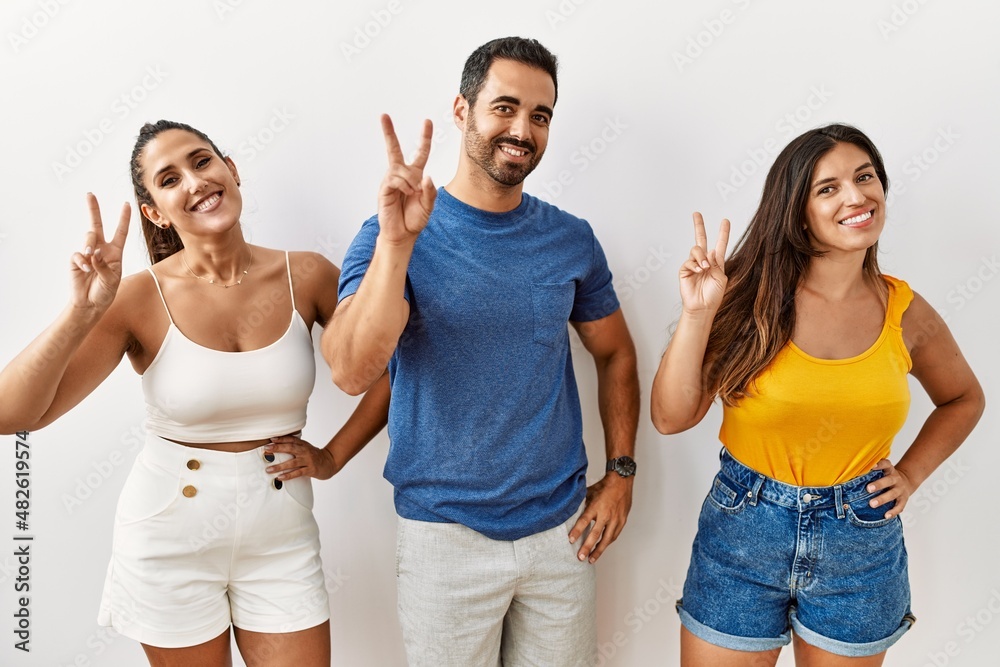 Group of young hispanic people standing over isolated background smiling looking to the camera showing fingers doing victory sign. number two.