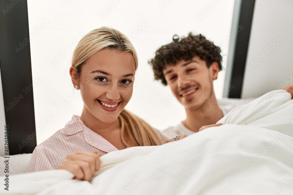 Young beautiful couple lying in bed and covering with blanket at home. Young beautiful couple lying in bed and covering with blanket at home.