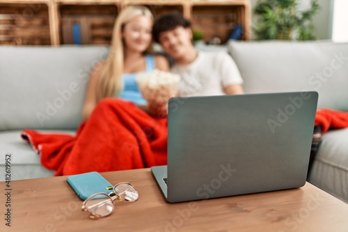 Young couple watching film and eating popcorn sitting on the sofa at home.