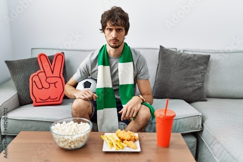 Young hispanic man football hooligan cheering game at home skeptic and nervous, frowning upset because of problem. negative person. © Krakenimages.com