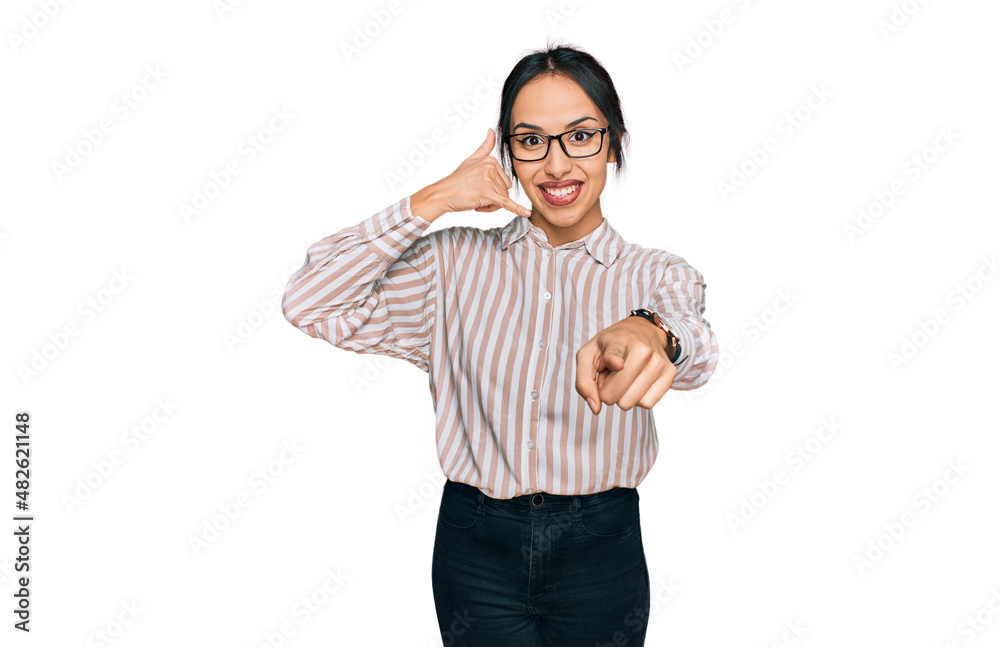 Naklejka premium Young hispanic girl wearing casual clothes and glasses smiling doing talking on the telephone gesture and pointing to you. call me.