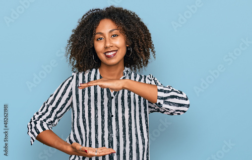 Young african american girl wearing casual clothes gesturing with hands showing big and large size sign, measure symbol. smiling looking at the camera. measuring concept. © Krakenimages.com
