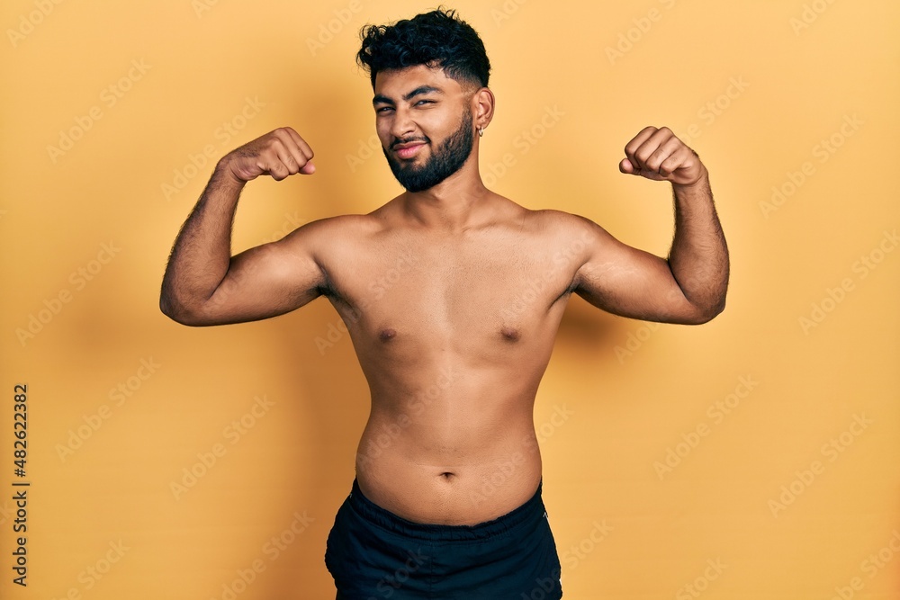 Arab man with beard wearing swimwear shirtless showing arms muscles smiling proud. fitness concept.