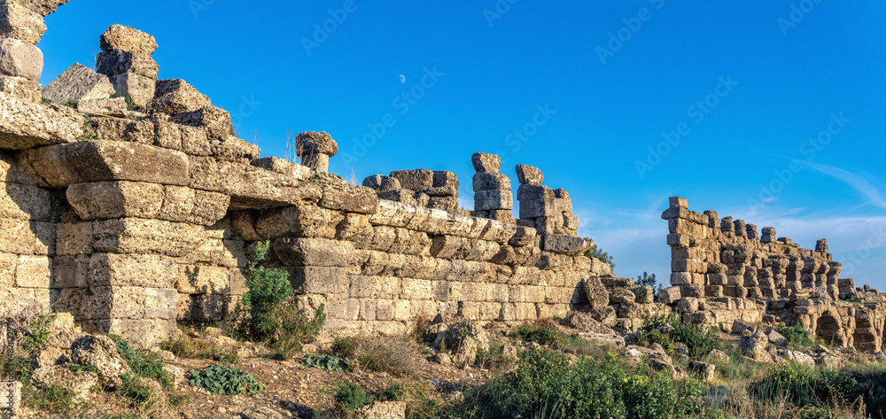 ruins of ancient city walls against the backdrop of the sky with moon in Side, Turkey