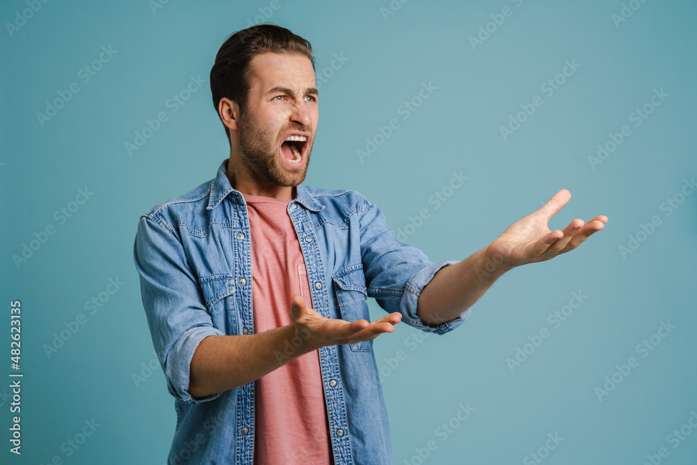 Young furious man wearing shirt gesturing and screaming at camera - obrazy, fototapety, plakaty 