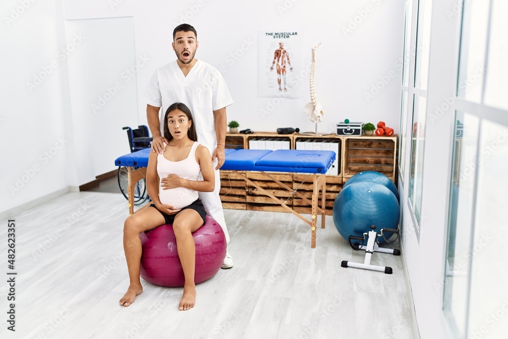 Fototapeta premium Young asian woman getting pregnancy class at physiotherapist clinic scared and amazed with open mouth for surprise, disbelief face