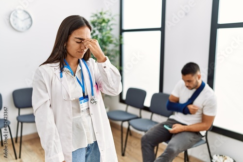 Young asian doctor woman at waiting room with a man with a broken arm tired rubbing nose and eyes feeling fatigue and headache. stress and frustration concept.