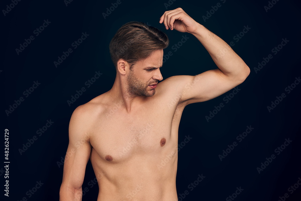 Handsome young man isolated. Portrait of shirtless muscular man is standing on dark blue background. Feel the smell of sweat. Men care concept.