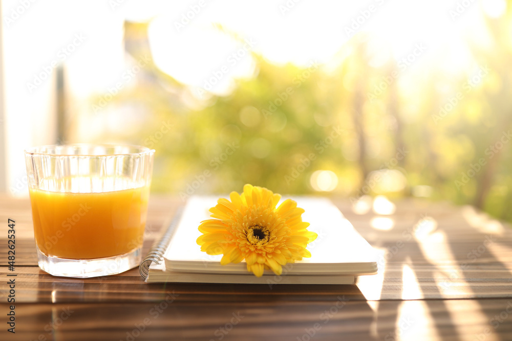 Mango juice glass cup and yellow gerbera flower and notebook