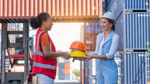 African american woman get safety helmet from Woman CEO cargo container warehouse on activity safety day, assign taske to foreman photo