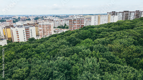 Aerial flight over large overgrown green wild forest overlooking city buildings
