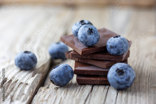 Dark chocolate stack and fresh organic blueberries on wooden table. Natural light, selective focus.