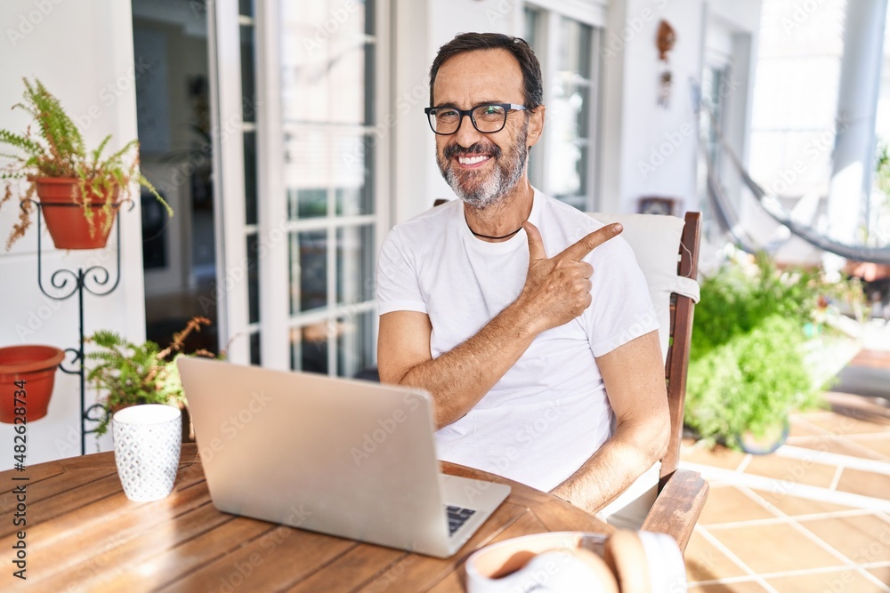 Middle age man using computer laptop at home cheerful with a smile on face pointing with hand and finger up to the side with happy and natural expression Middle age man using computer laptop at home cheerful with a smile on face pointing with hand and finger up to the side with happy and natural expression