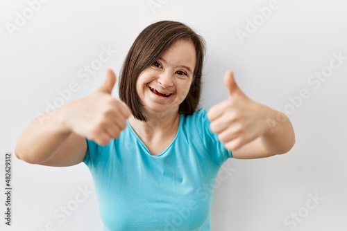 Young down syndrome woman standing over isolated background success sign doing positive gesture with hand  thumbs up smiling and happy. cheerful expression and winner gesture.
