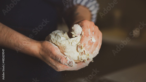 A man in a blue apron kneads bread dough with his hands. Home cooking. Cooking dough in the kitchen.