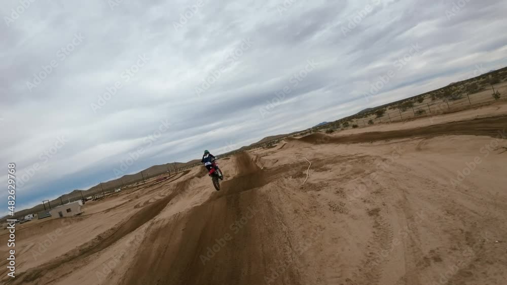 Following an off-road motocross bike as it takes a jump on a racetrack with backdrop of the Mojave Desert - aerial first-person drone in slow motion Following an off-road motocross bike as it takes a jump on a racetrack with backdrop of the Mojave Desert - aerial first-person drone in slow motion
